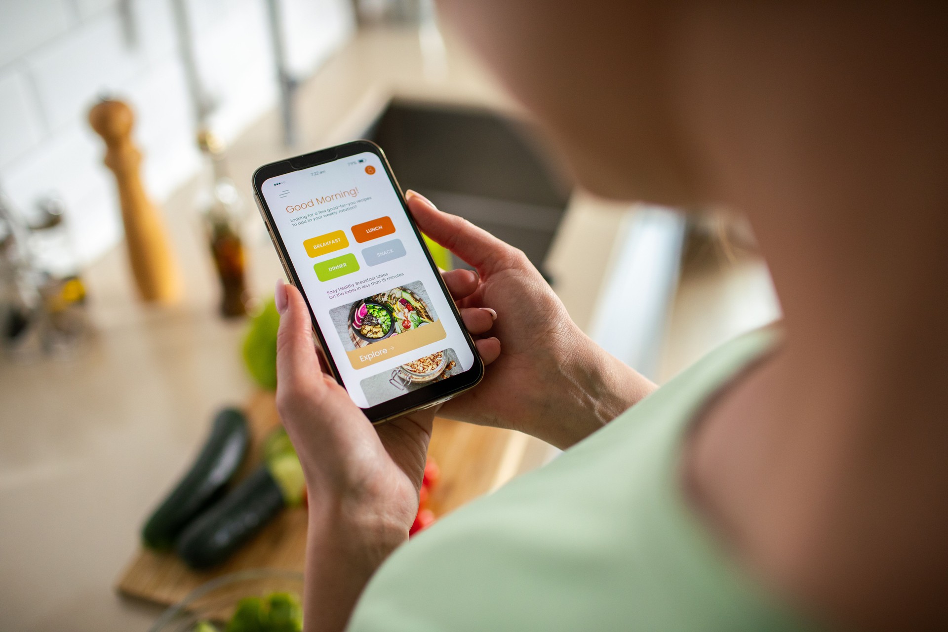 Young woman using a diet app on her phone while preparing a healthy food dish at home