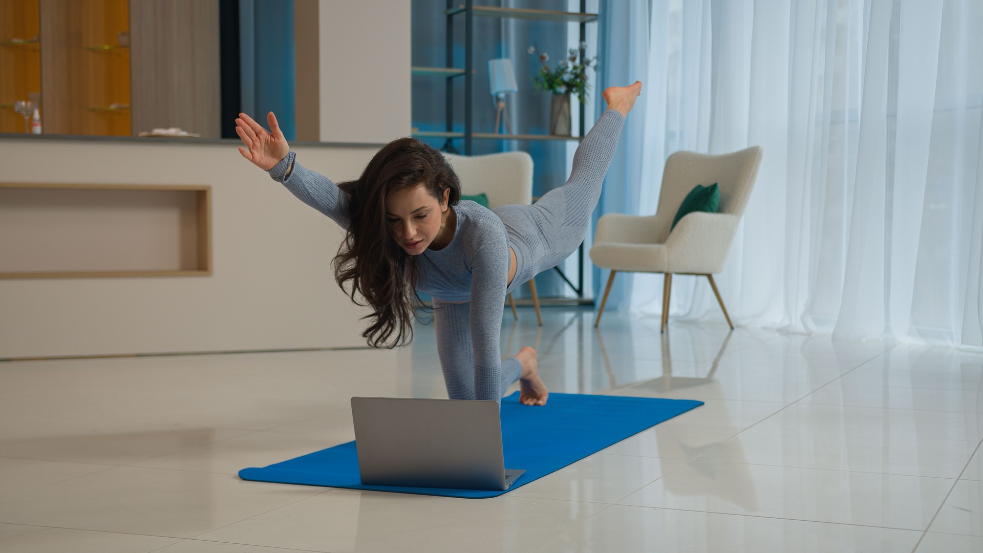 Yoga class with laptop workout video tutorial online training at home fit Caucasian woman sport trainer girl yogi female sportswoman doing exercise raise leg hand learning asana fitness pilates on mat